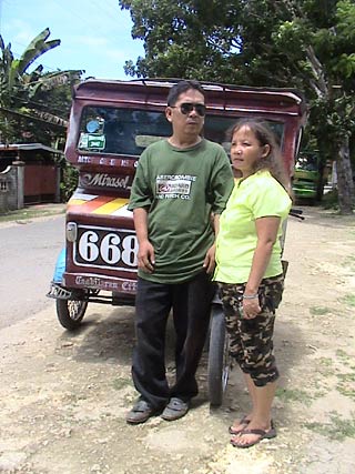 Nong Lumi and his wife Laureana standing in front of his tricycle.